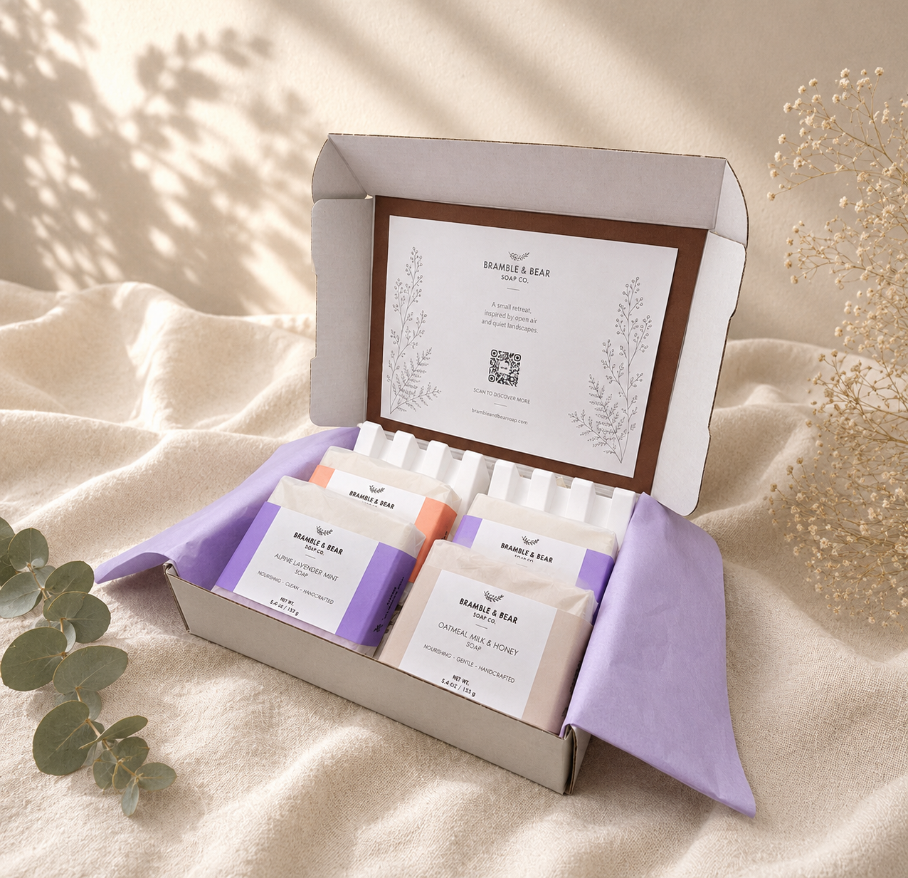 Open Bramble & Bear Deluxe Soap & Tray Ritual Set displaying four signature soaps and two soap trays in a white gift box with lavender tissue, styled on warm ivory linen with eucalyptus and dried flowers.