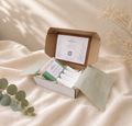 Open small Bramble & Bear spa gift box with soap and white soap dish, arranged on ivory linen with eucalyptus and dried botanicals.