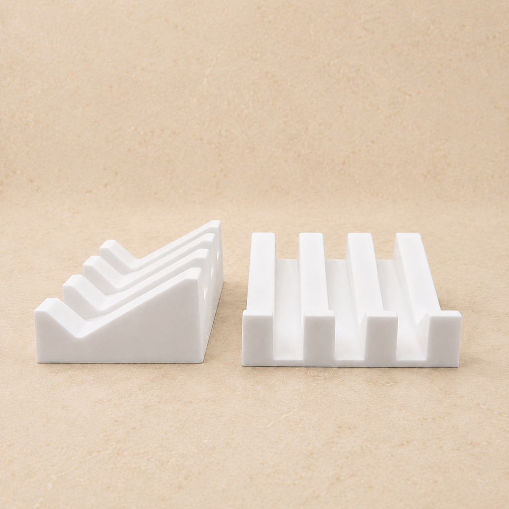 Two ridged soap dishes shown from the side on a beige stone countertop, highlighting the sloped design and raised drainage ridges.
