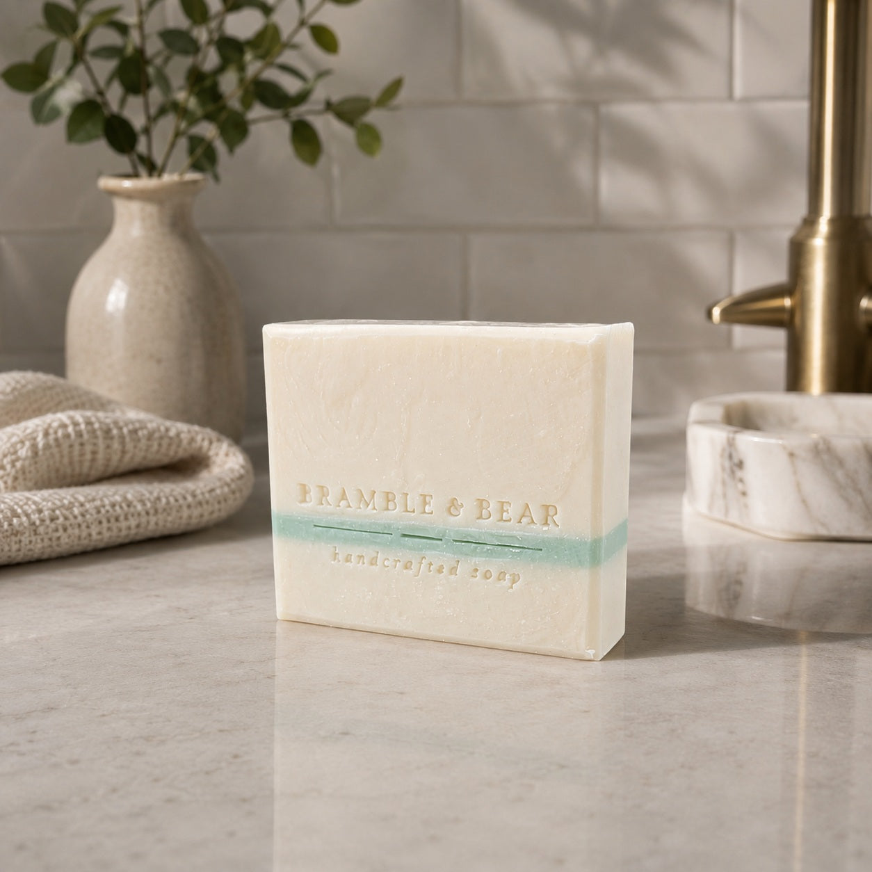 Apothecary Rice Soap standing on a stone vanity with folded towels, greenery, and a softly lit bathroom. 