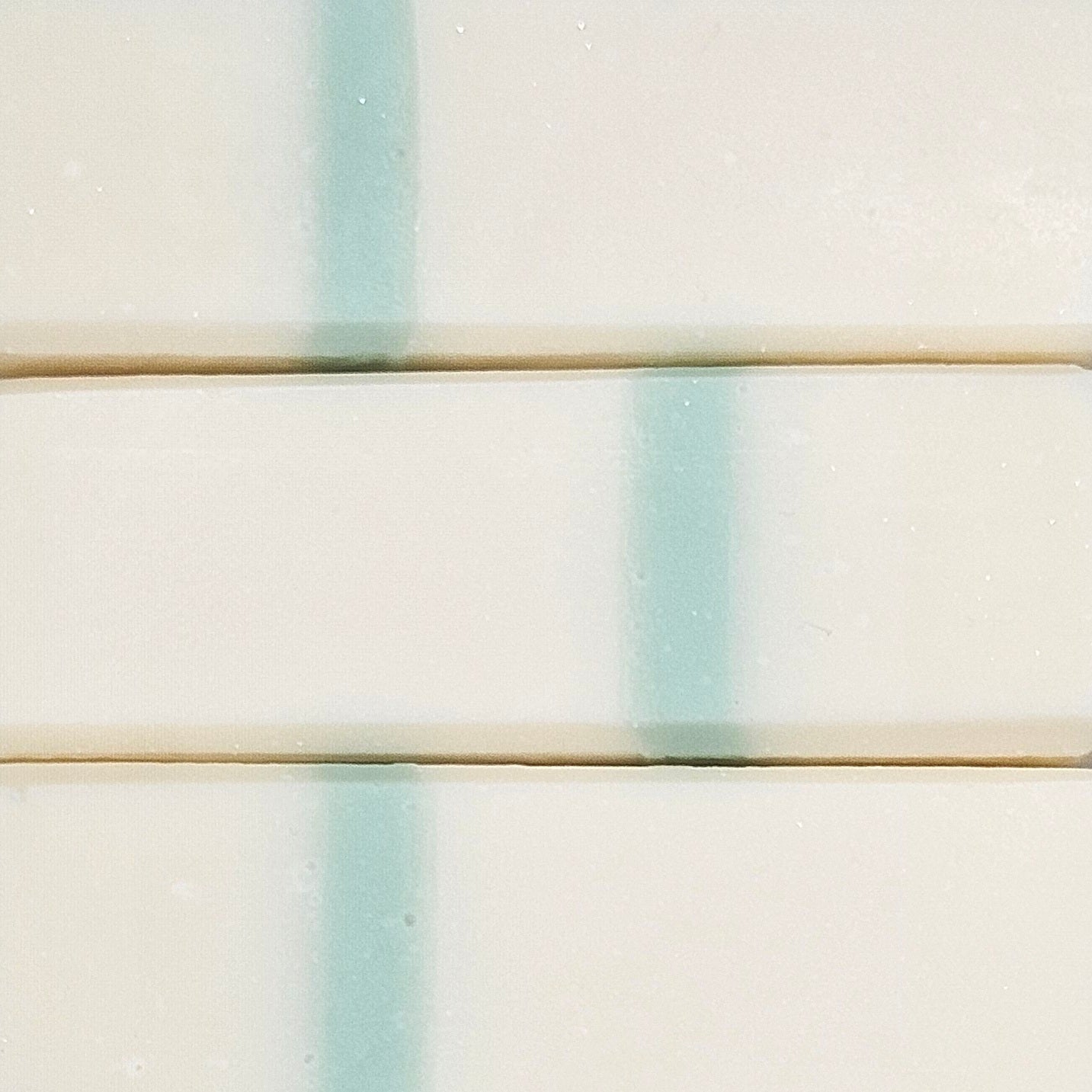 Macro view of stacked ivory Apothecary Rice Soap bars showing the pale aqua stripe and handmade texture. 