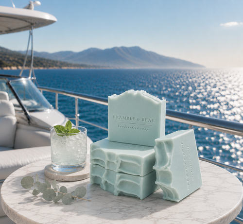 Coastal Eucalyptus Mist handmade soaps stacked on a marble yacht table with soft aqua sea-glass tones, wave-carved textures, eucalyptus, a mint drink, and a sunlit ocean background.