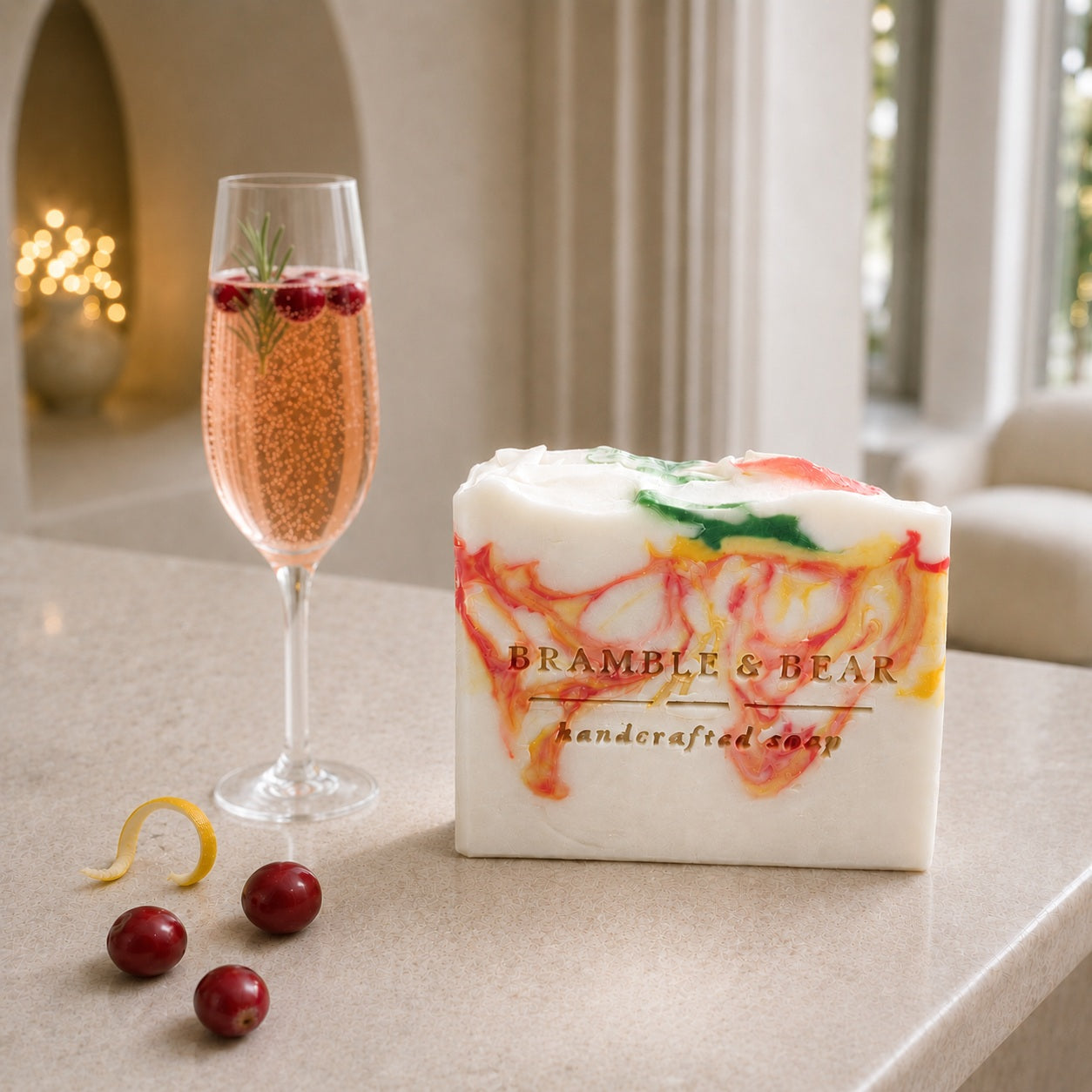 A Bramble & Bear Cranberry Prosecco Spritz soap bar with coral, yellow, and green marbling sits beside three cranberries and a curled citrus rind on a pale stone counter in an elegant ivory hotel lounge.