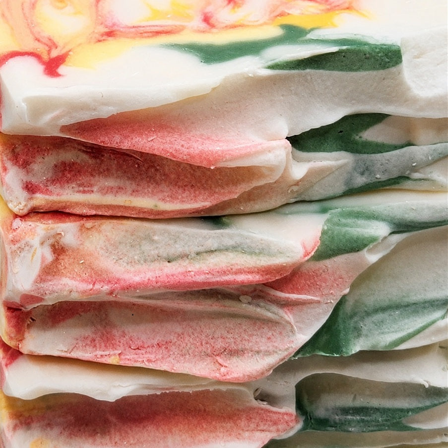 Close-up of stacked Bramble & Bear Cranberry Prosecco Spritz soaps, highlighting their irregular layered texture and coral, yellow, green, and cream marbling.