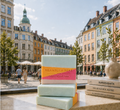 Three Bramble & Bear Copenhagen Summer soaps stacked before a sunny Copenhagen city square. 