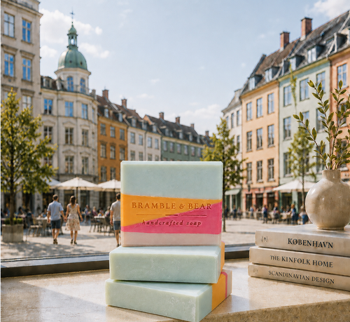 Three Bramble & Bear Copenhagen Summer soaps stacked before a sunny Copenhagen city square. 