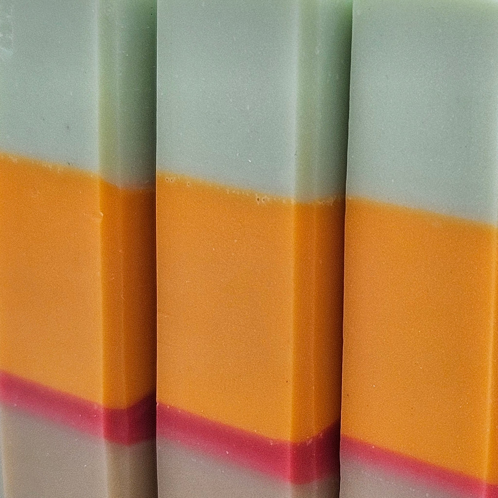 Close-up of three Copenhagen Summer soap bars showing pale mint, orange and raspberry layers and handmade texture. 