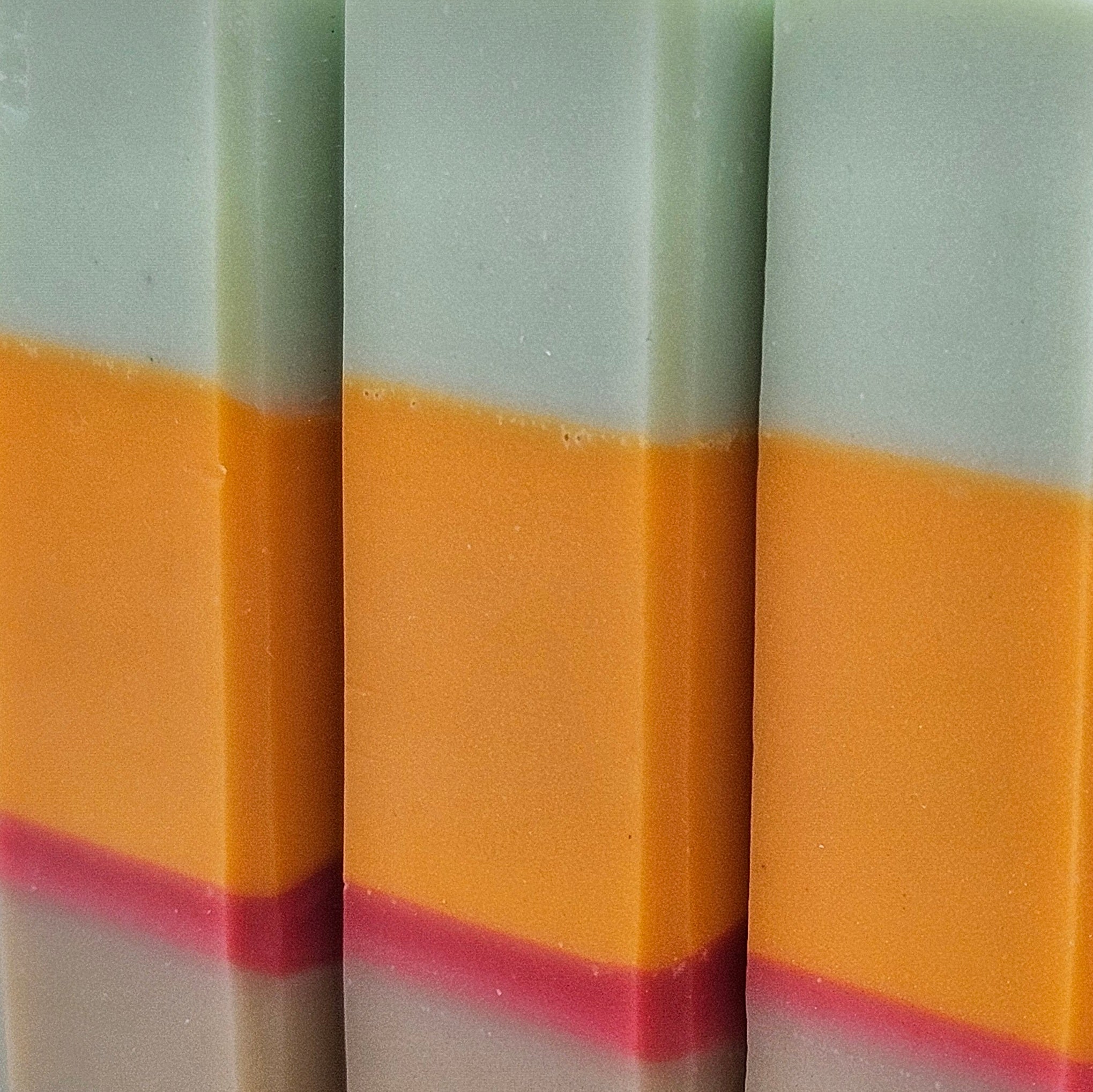 Close-up of three Copenhagen Summer soap bars showing pale mint, orange and raspberry layers and handmade texture. 