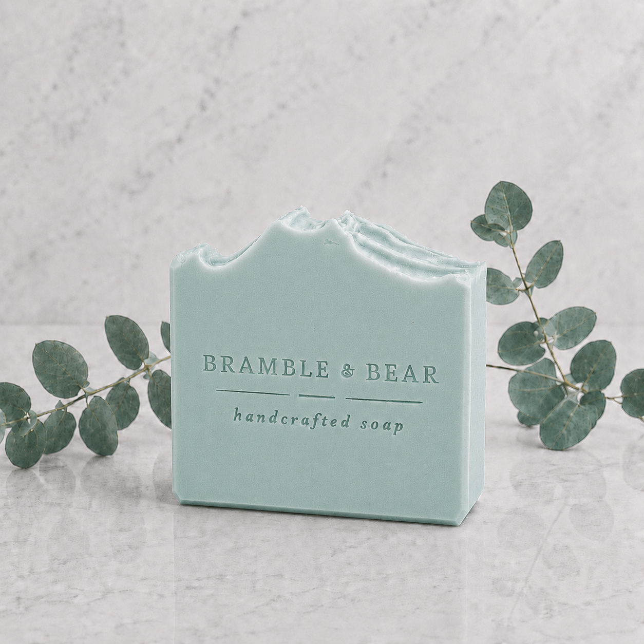 Coastal Eucalyptus Mist handmade soap standing on a marble surface with a soft aqua base, creamy upper layer, eucalyptus sprigs, and a clean spa-style botanical setting.