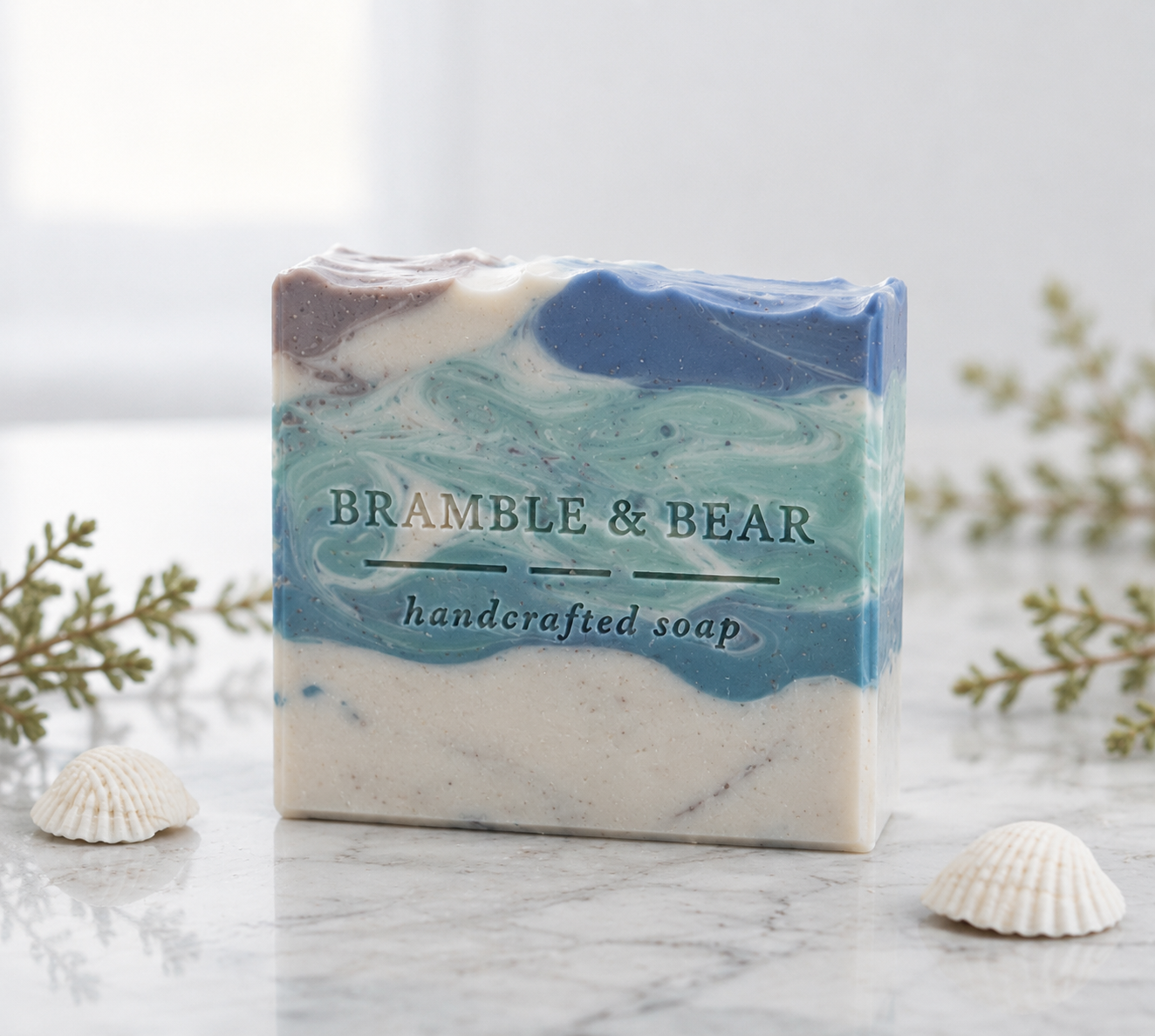 Coastal Rain Fog handmade soap standing on a light marble surface with blue and white ocean-like swirls, a shell embed, small seashells, and soft greenery in the background.