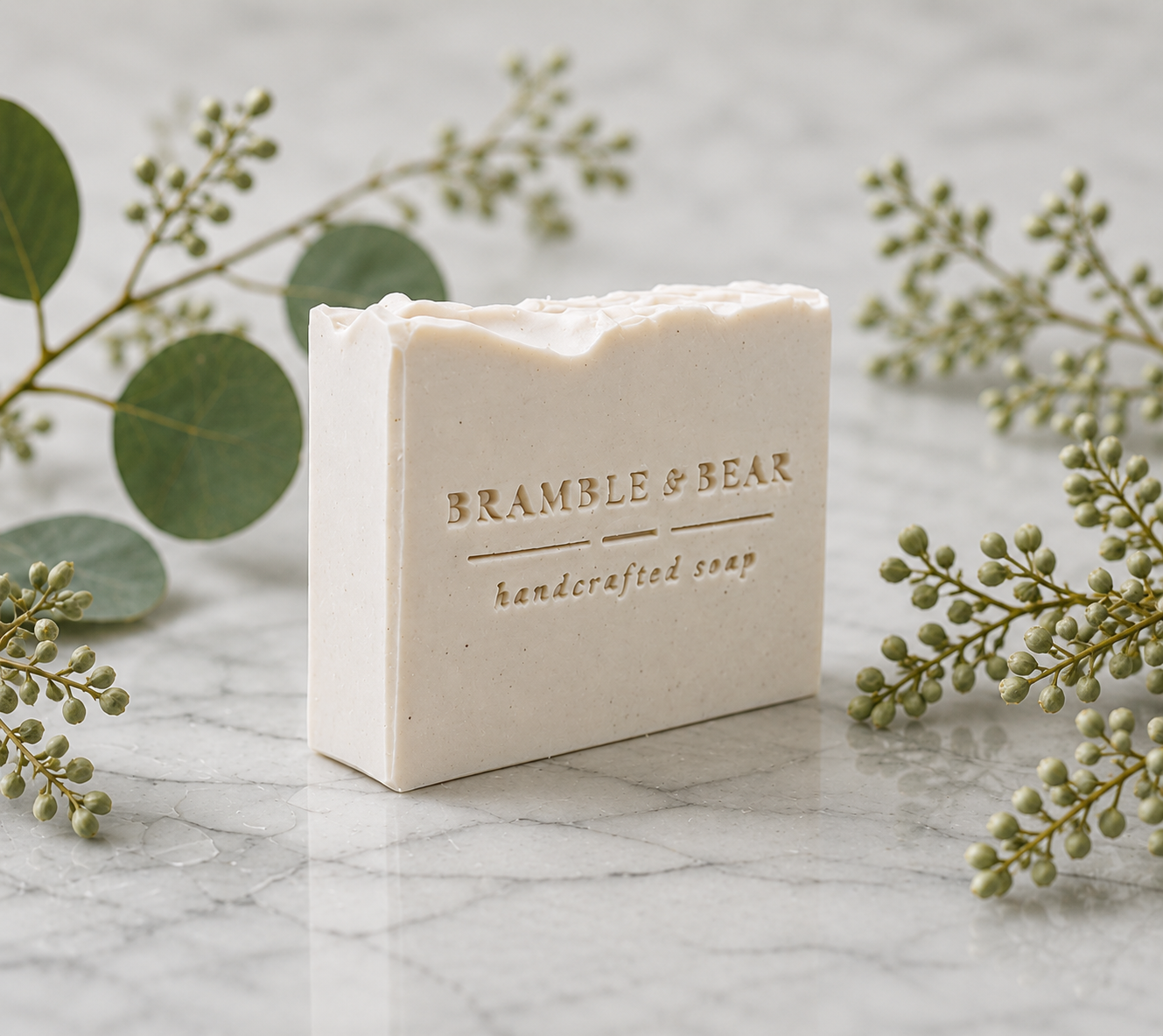 Single Honey Oatmeal Grove soap bar on a marble surface with minimal green botanicals around it, showing the Bramble & Bear handcrafted soap stamp on the front.