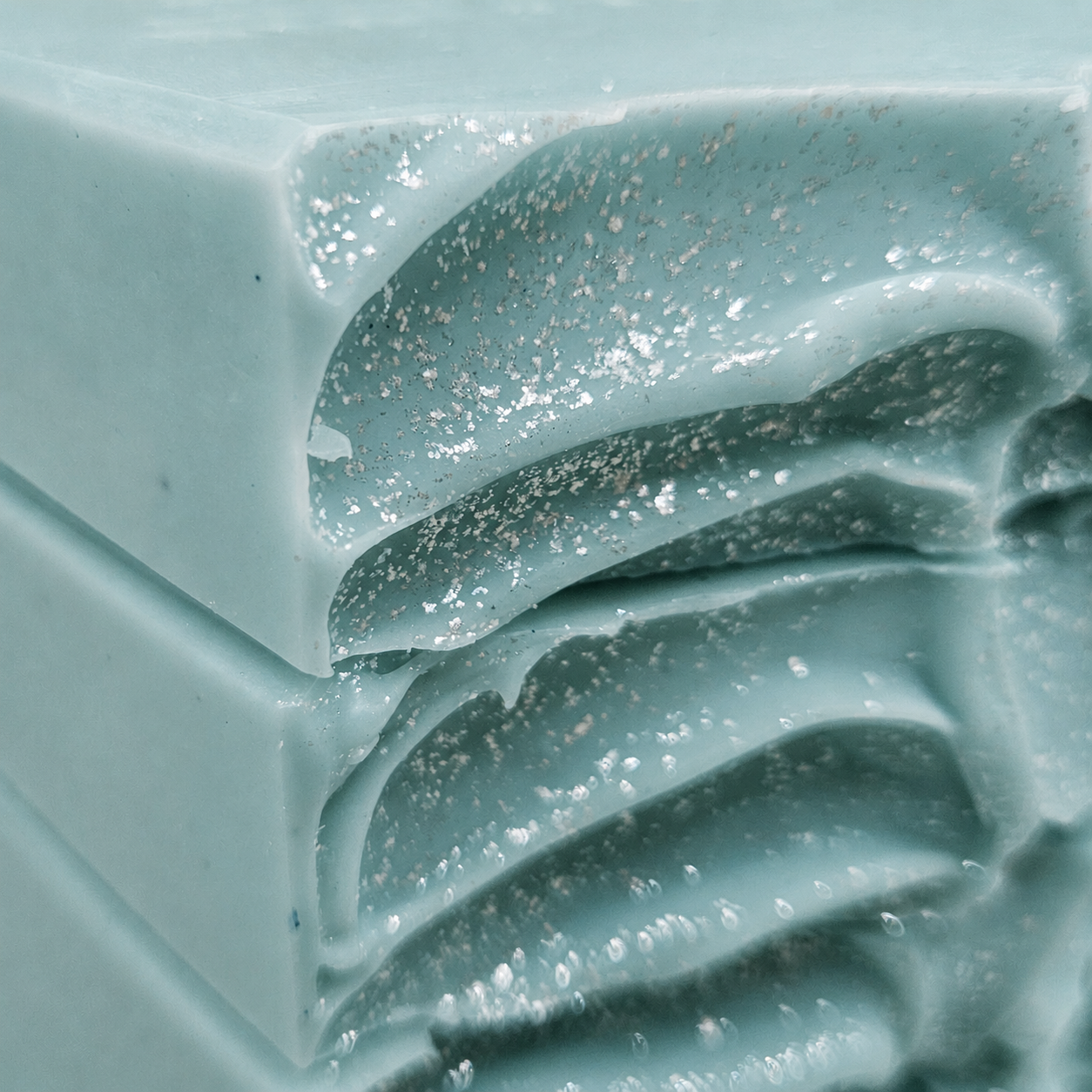 Close-up of Coastal Eucalyptus Mist handmade soap showing aqua sea-glass color, wave-carved texture, silver speckled details, and handmade cold-process surface.