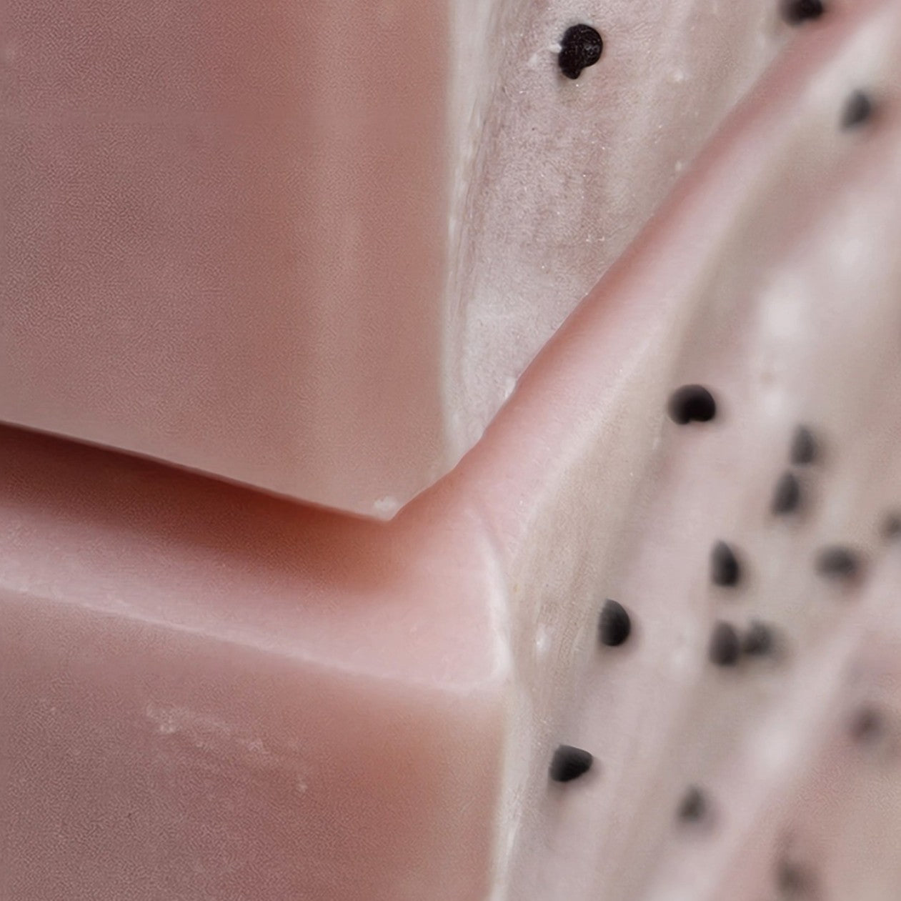 Close-up of Wild Rose Meadow soap showing smooth pink soap texture, soft edges, and fine dark botanical speckles.