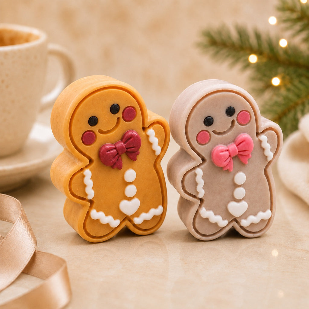 Frosted Pumpkin Apple and Frosted Gingerbread Cutie soaps standing together on warm stone with a cream mug, champagne ribbon, and softly blurred Christmas greenery and lights.