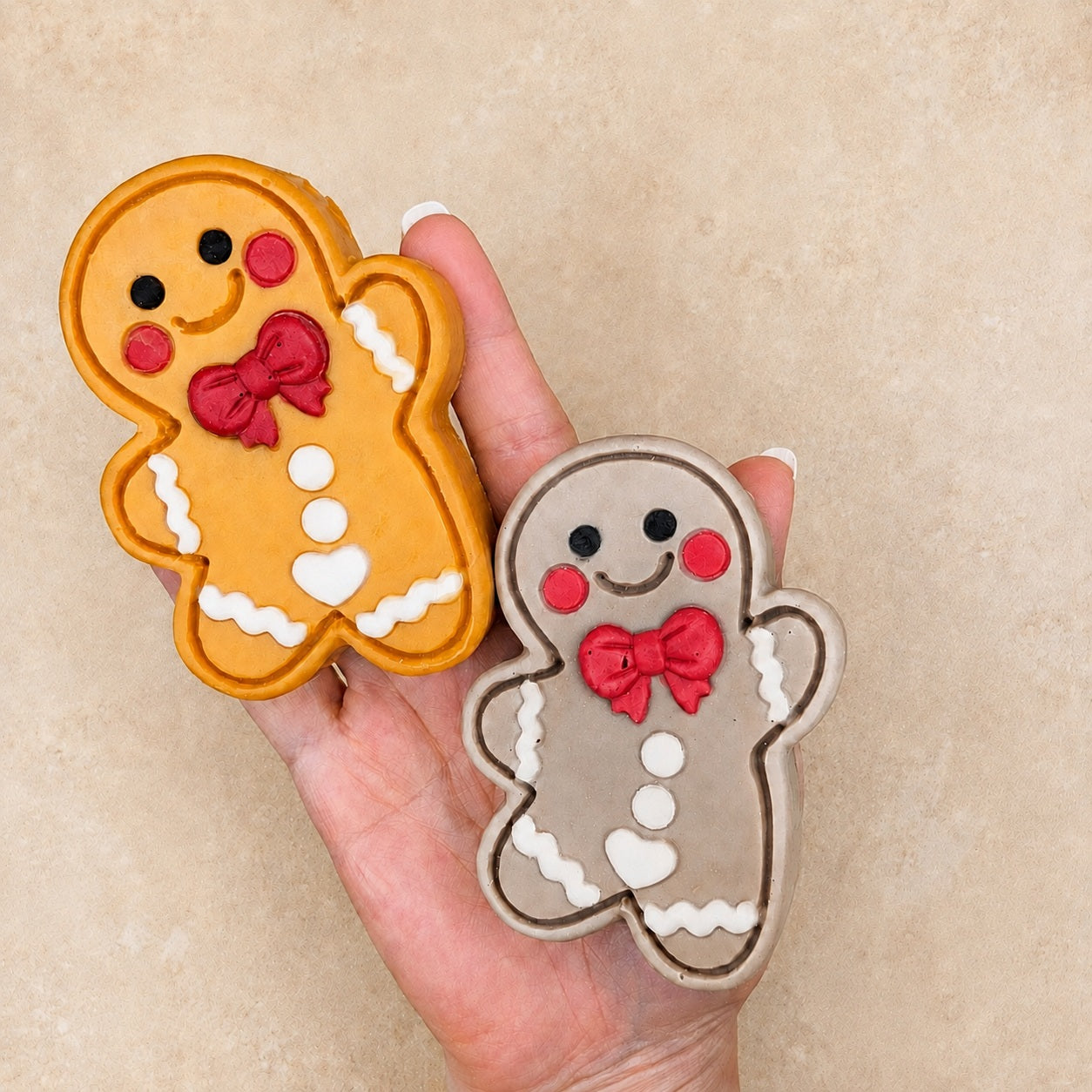 Golden Frosted Pumpkin Apple and taupe Frosted Gingerbread Cutie soaps held together in one hand against a plain cream stone background to show their size and handcrafted details.