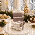 Frosted Gingerbread Cream soaps stacked on warm marble amid glowing Christmas greenery and an elegant winter dessert table.