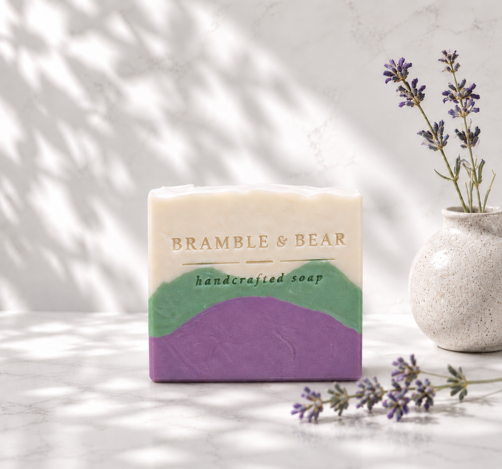 Single Alpine Lavender Mint soap bar in a bright spa setting with soft botanical shadows, lavender sprigs, and the Bramble & Bear stamp on the front.