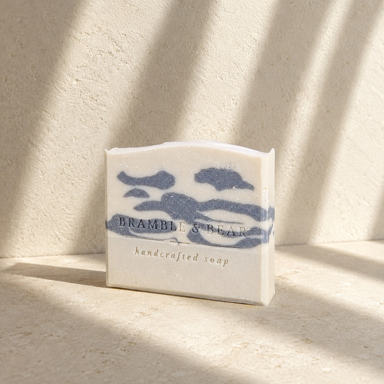 Silver Birch Crossing soap illuminated by soft sunlight and sweeping shadows on warm greige stone.