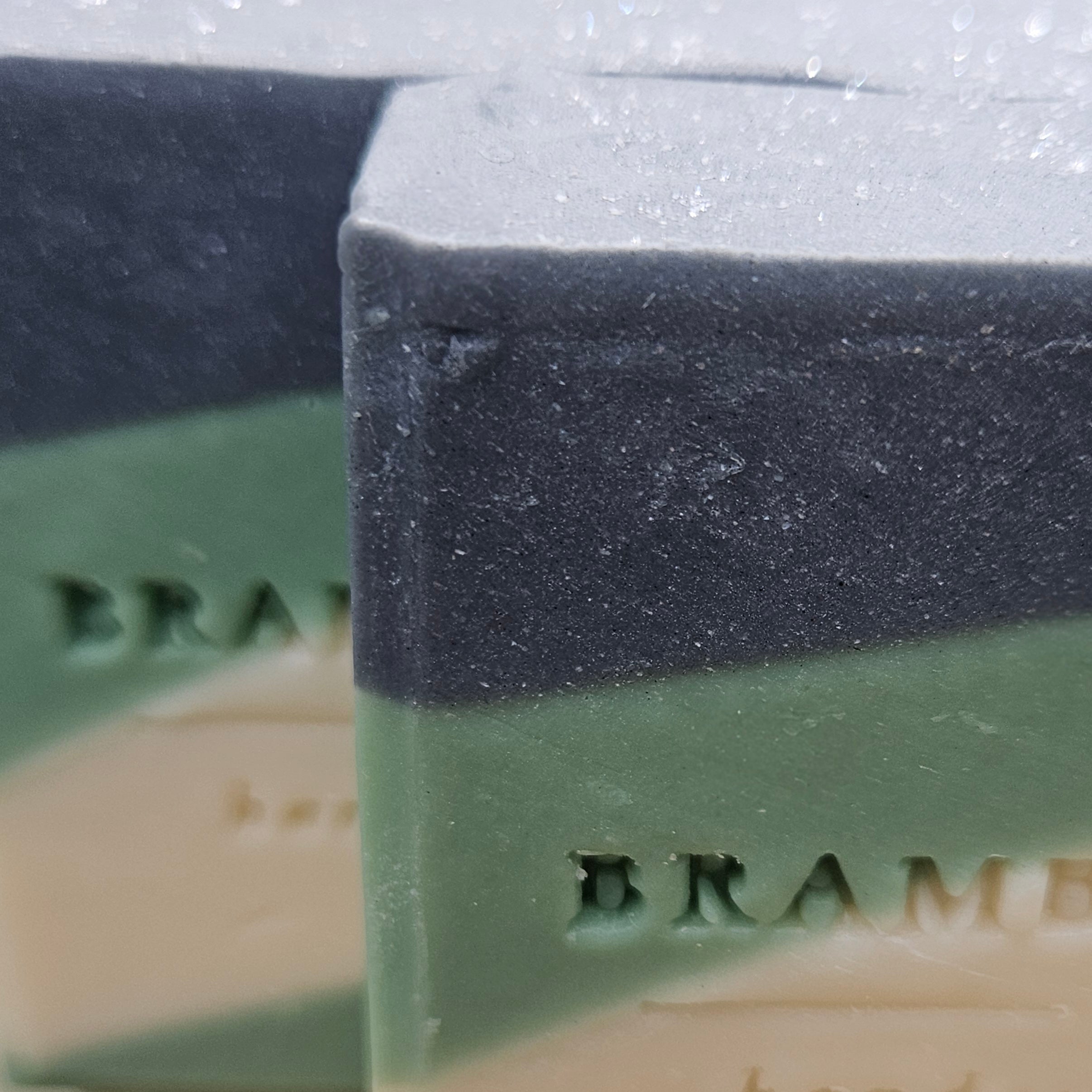 Close-up of Silent Evergreen Night soap bars showing their handmade texture and layered charcoal-gray, forest-green, and ivory design.